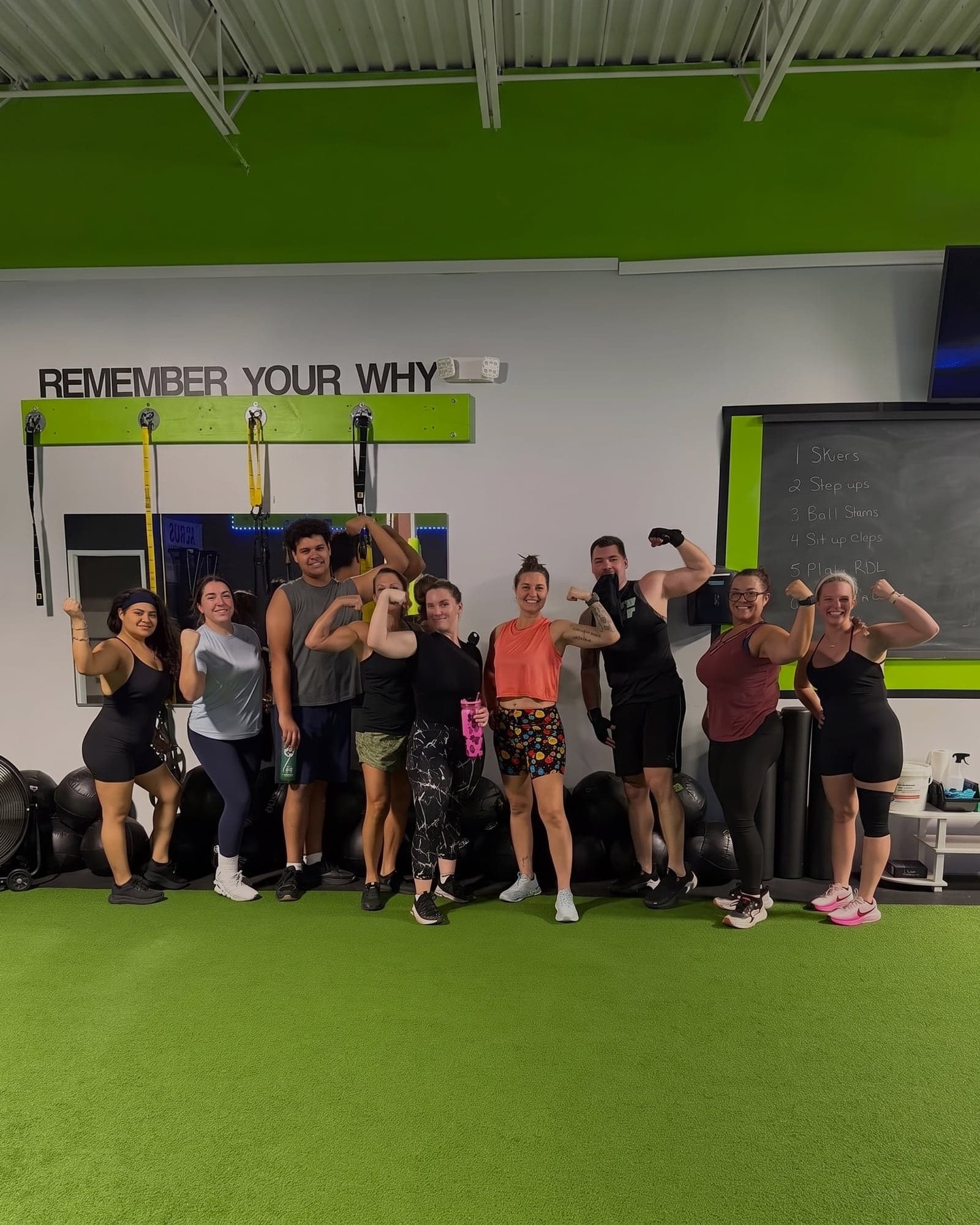 The 6:30 class flexing together on the turf under the gym's REMEMBER YOUR WHY sign